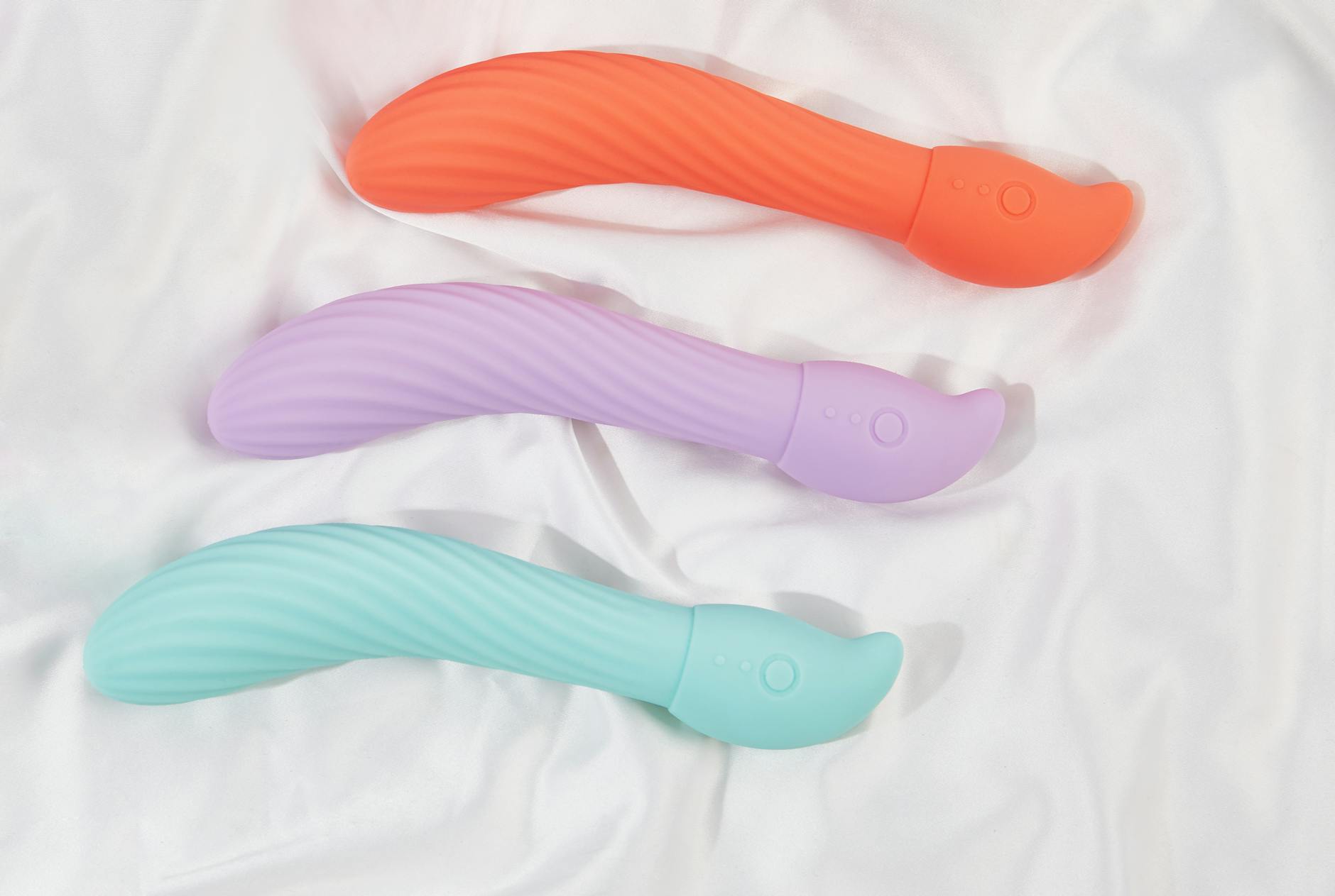 Mano sosteniendo un vibrador de succión clitoral de color brillante sobre fondo blanco, mostrando la forma ergonómica del diseño